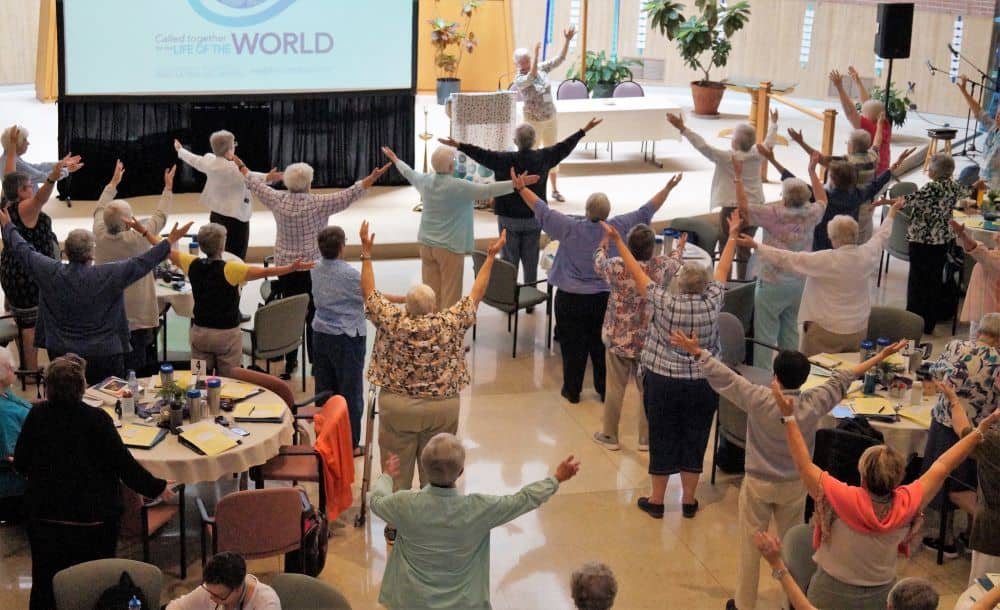 A photo from above shows a large group of sisters with their arms extended over their heads doing tai chi