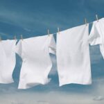 Clean white clothes and towels hang from a clothesline against a blue sky