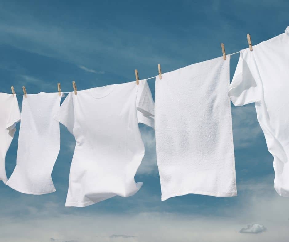 Clean white clothes and towels hang from a clothesline against a blue sky