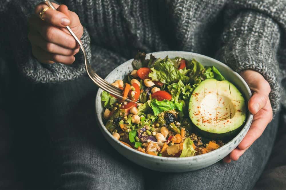 Hands holding a large bowl of mixed vegetables and grains
