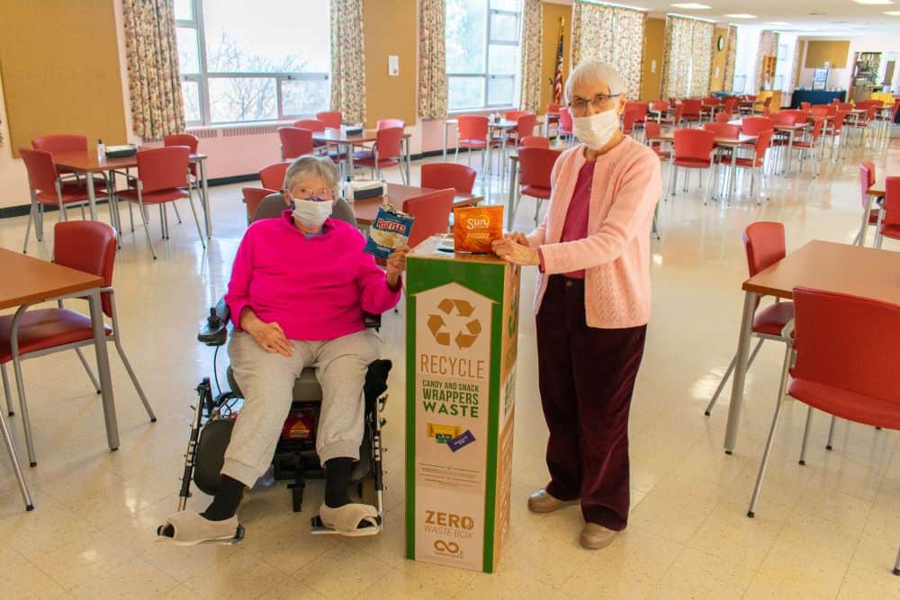 Two sisters pose as they dispose of potato chip bags in a TerraCycle box