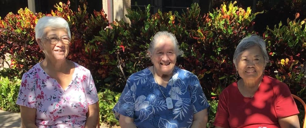 Sisters Roselani Enomoto, Sara Sanders and Eva Messina sit together outside in front of some bushes