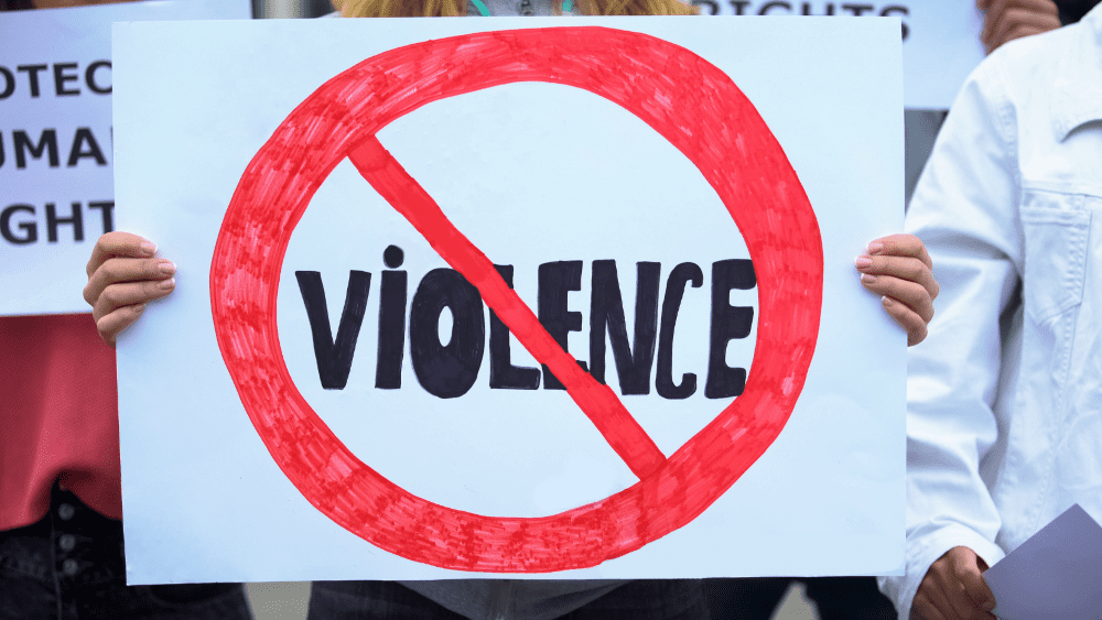 Someone at a rally holds up a sign with the word "violence" in a red circle with a strikeout line through it
