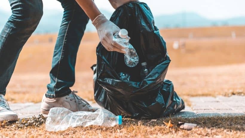 A person picks up plastic litter and puts it into a trash bag
