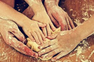 Five hands from different people work together to knead bread dough