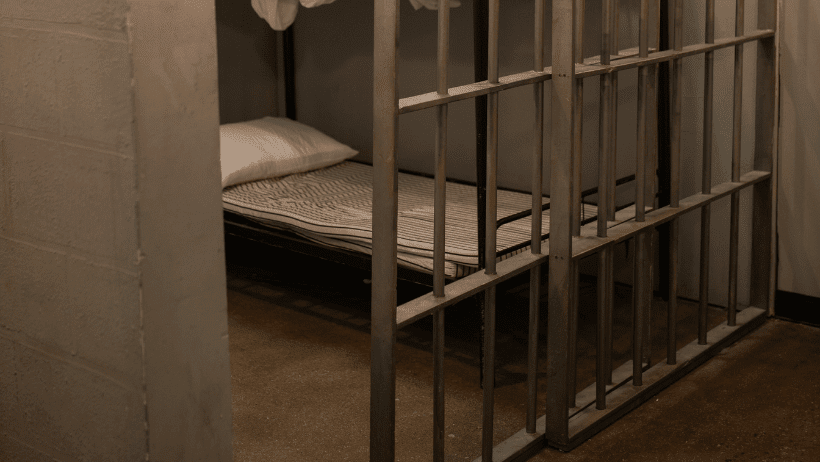 A bed in a prison cell, viewed beyond the bars