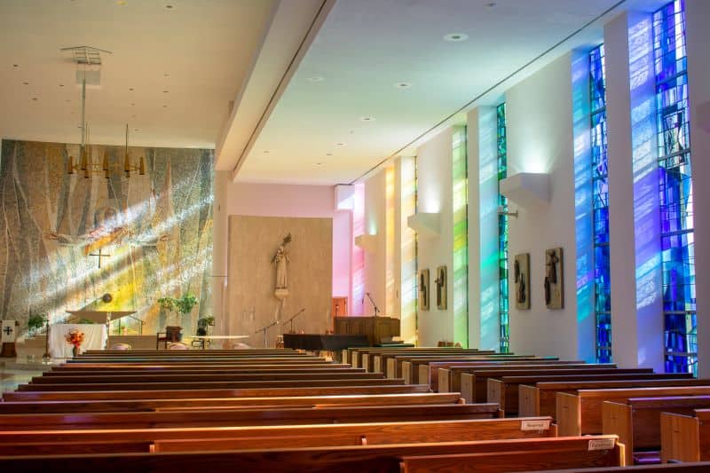 Light streams through the rainbow colored stained glass windows into the Albany chapel with a mosaic of the risen Christ in the background