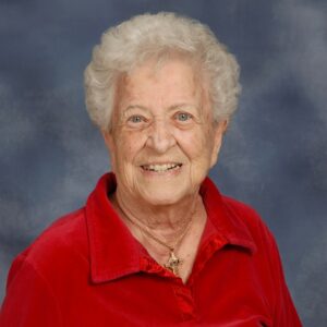 Headshot of Sister Alice Roberta Benzing in a red shirt with a blue background