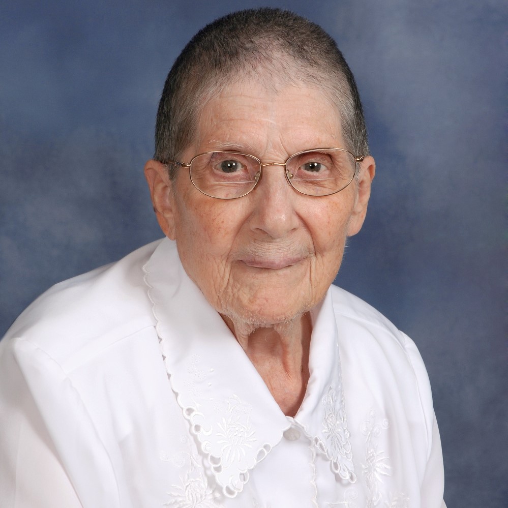 Sr. Marth Wachtel wearing a white blouse and glasses with a blue background.