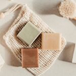 Brown, green and tan bars of soap sit on top of a soap saver bag of unbleached cotton mesh.