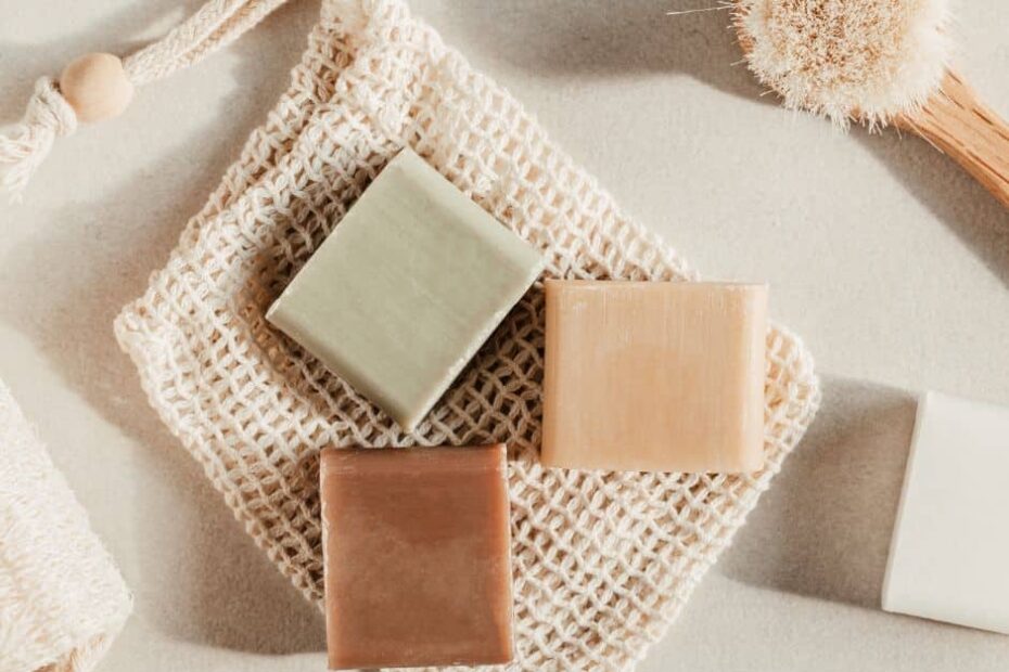 Brown, green and tan bars of soap sit on top of a soap saver bag of unbleached cotton mesh.