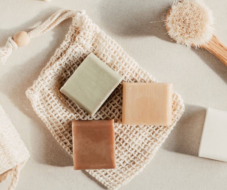 Brown, green and tan bars of soap sit on top of a soap saver bag of unbleached cotton mesh.