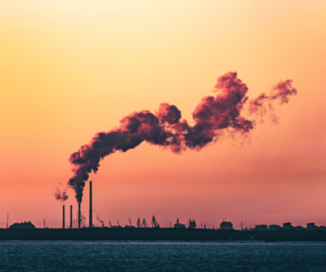 A dark billowing cloud is emitted by a smokestack in front of a beautiful sunset sky