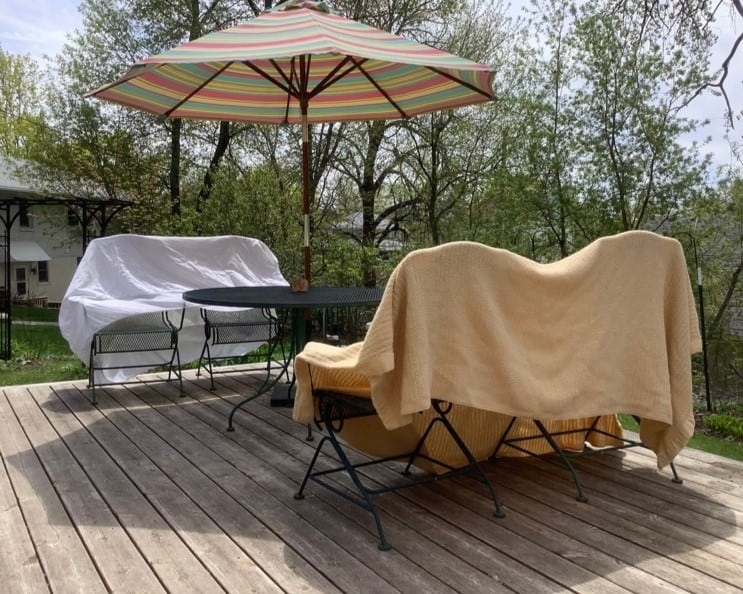 A sheet is stretched out over one bench and a blanket over another as they dry outside on a patio.