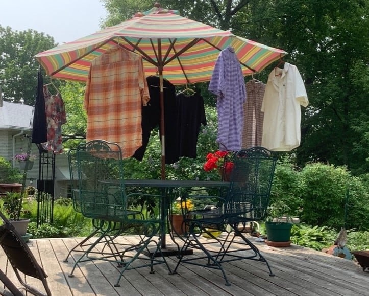 A patio umbrella supports four button-down shirts hanging from hangers