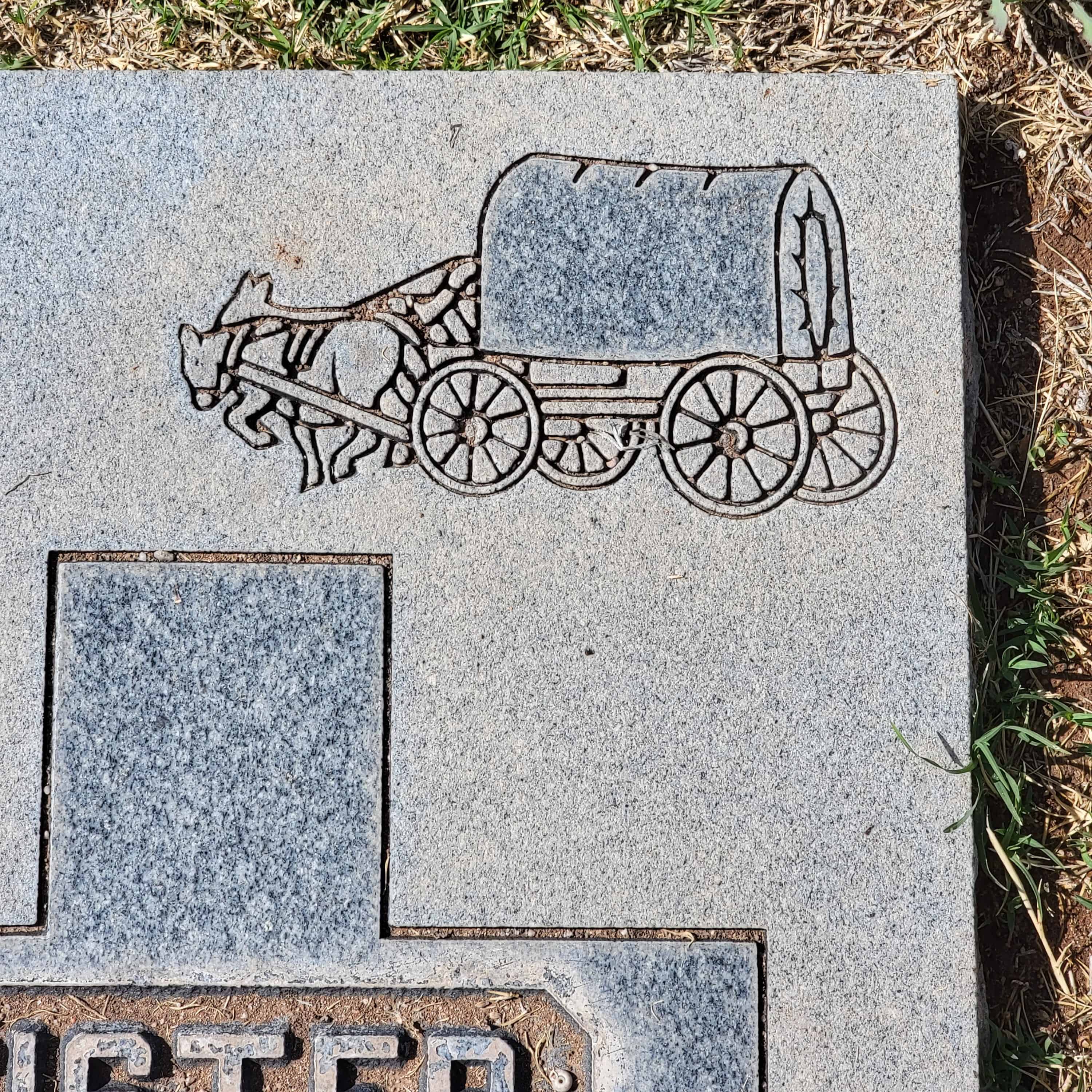 A covered wagon is carved into the top corner of a tombstone
