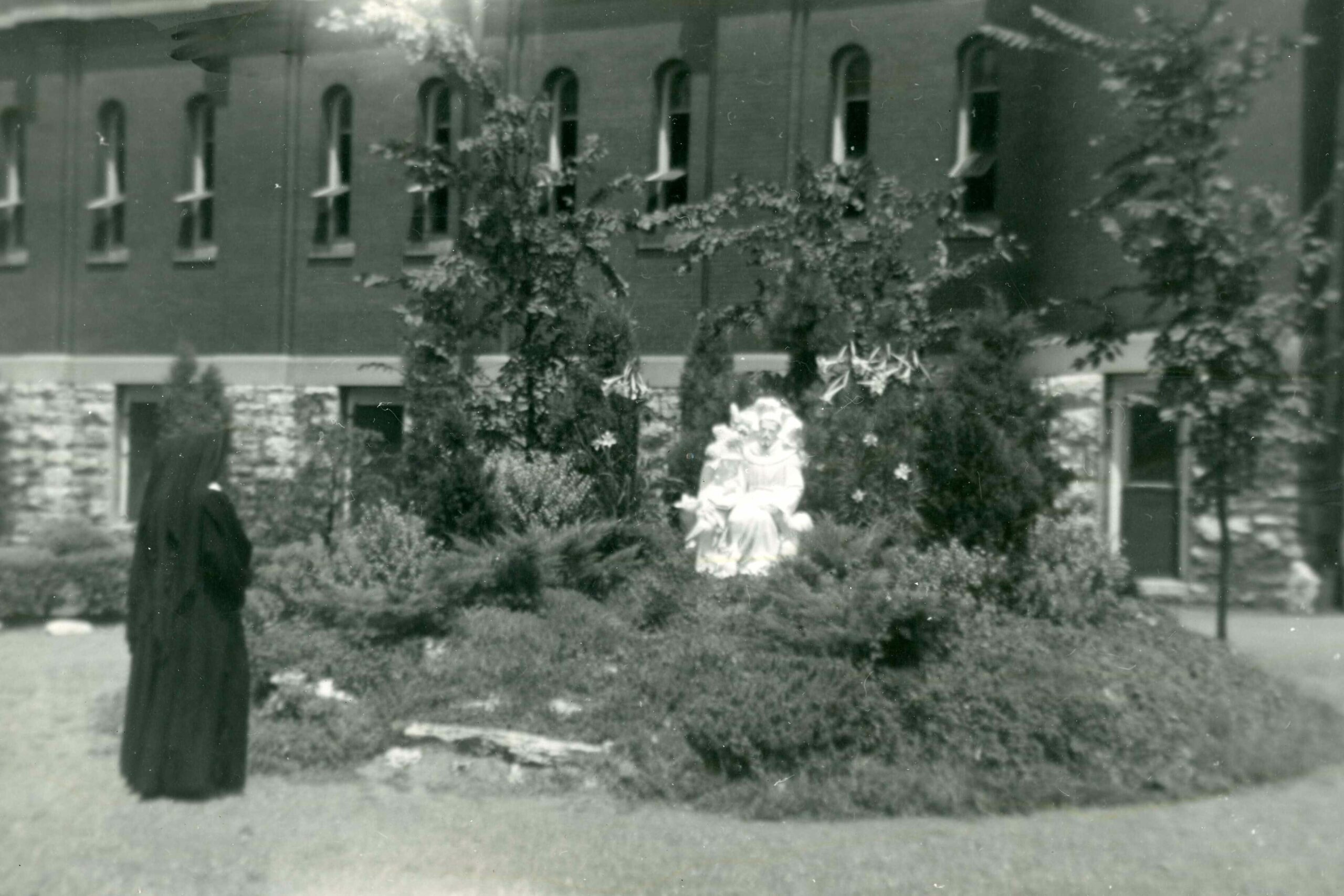 Black and white photo of a Sister of St. Joseph of Carondelet, Mother Pius Neenan, standing in front of the shrine of St. Francis of Assisi.