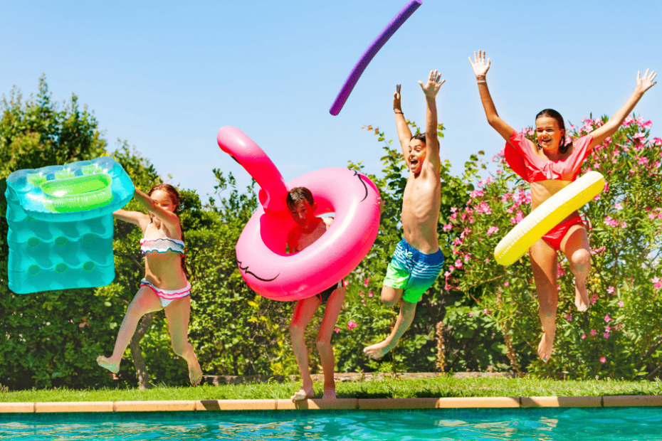 Four kids jumping into a pool holding pool rings and pool noodles.