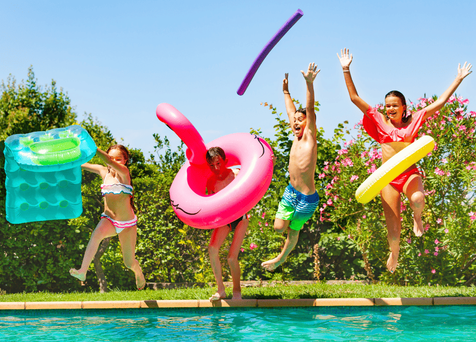 Four kids jumping into a pool holding pool rings and pool noodles.