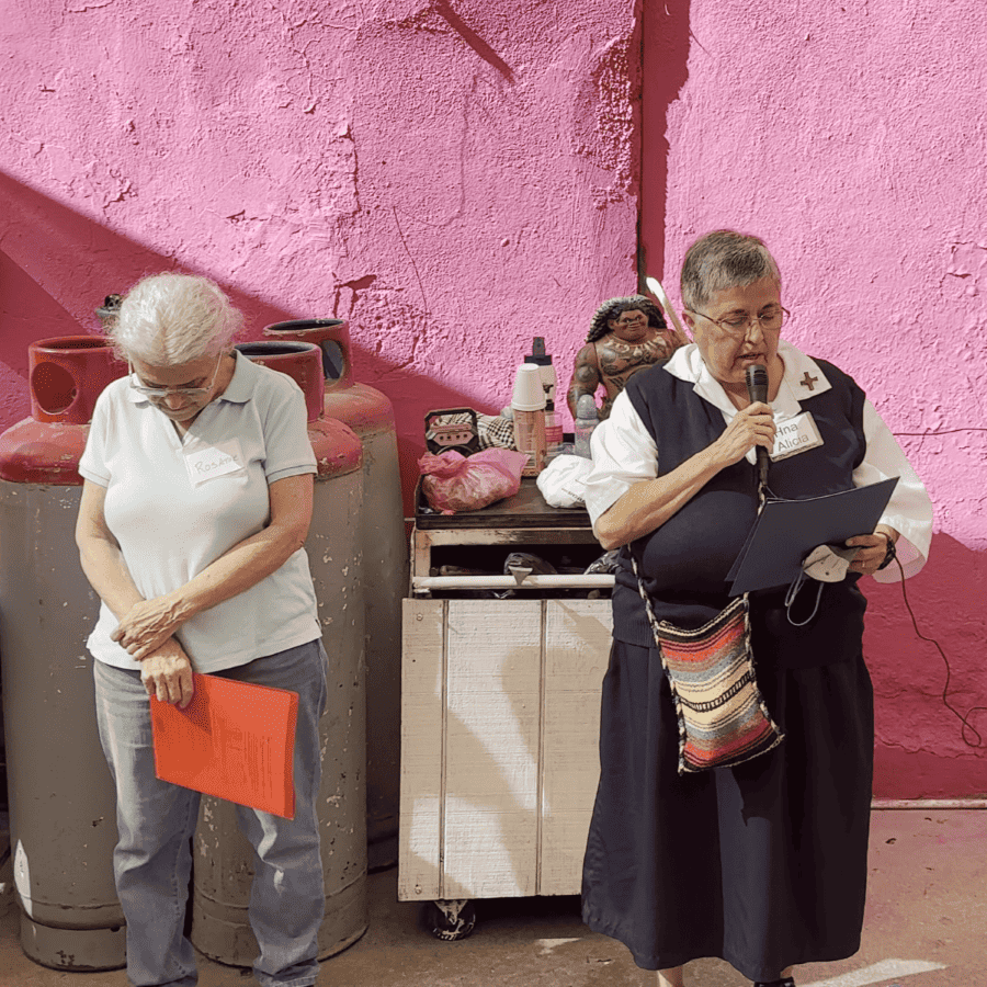 Sisters Rosanne Belpedio and Alicia Rivera in front of a pink wall leading a blessing