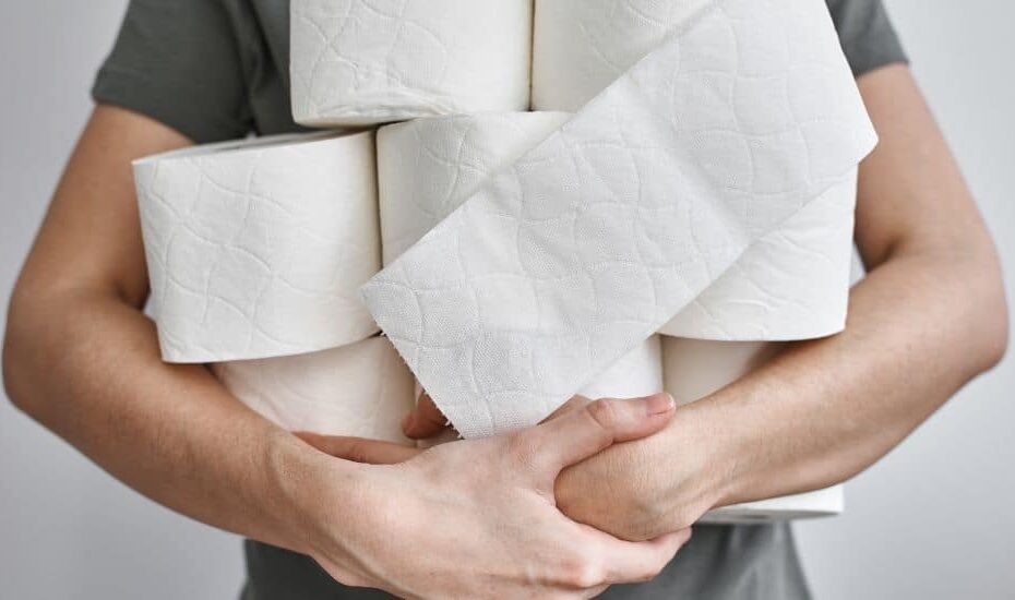 A person holds at least eight rolls of toilet paper haphazardly in their arms