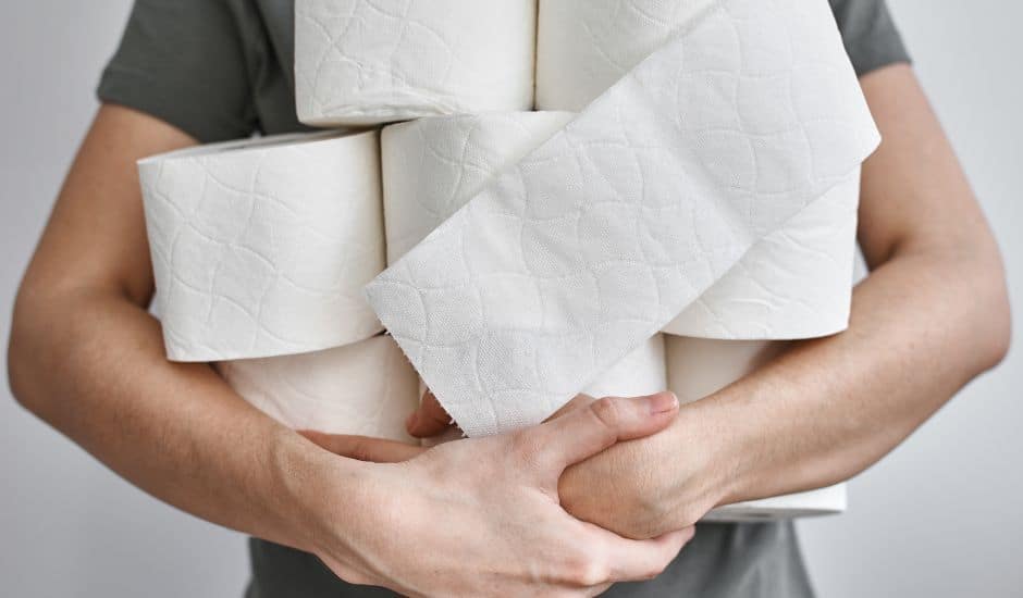 A person holds at least eight rolls of toilet paper haphazardly in their arms