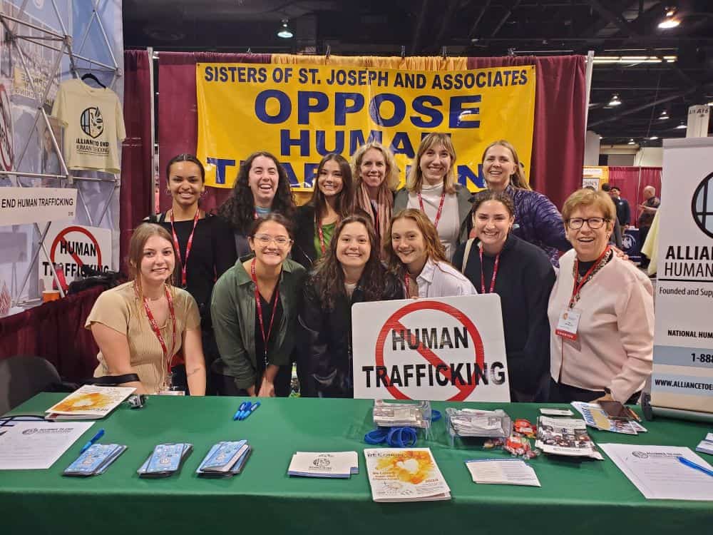 Sisters Sally Koch and Judy Molosky posing for a group photo with ten Saint Joseph Workers at the Alliance to End Human Trafficking booth
