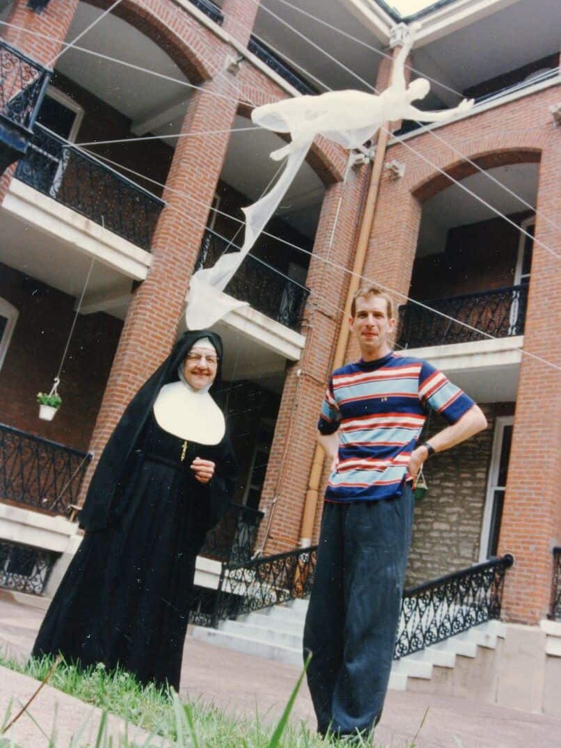 A man and a woman in a habit standing under a floating sculpture