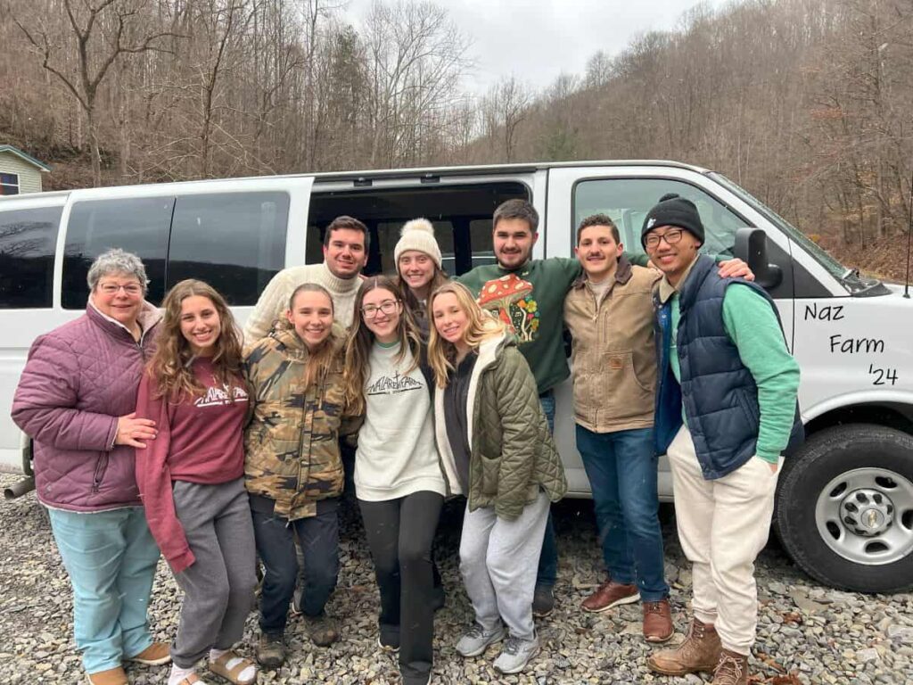 Sister Rose Casaleno and a group of nine retreatants from Binghamton University taking a group photo in front of a van