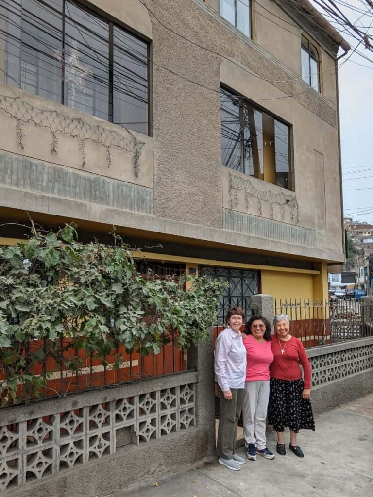 Three women stand together in front of a three story house.