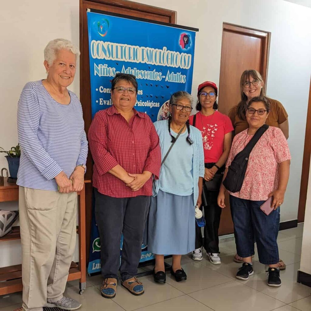 Six women stand in front of a banner about psychological service offered by Sister Ruth Matos.