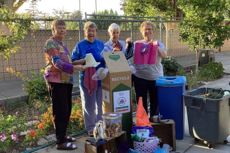 Four women stand next to a pile of collected hard to recycle objects.