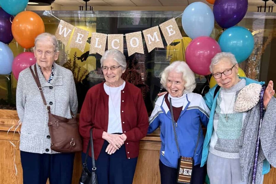 A group of four sisters stand in front of a welcome banner with bunches of balloons