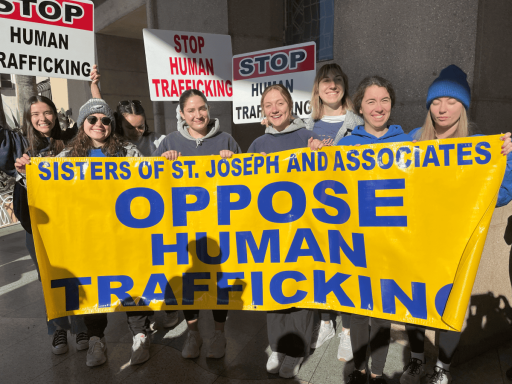 Eight women holding signs that read "stop human trafficking" and a banner that reads "Sisters of St. Joseph and Associates Oppose Human Trafficking"