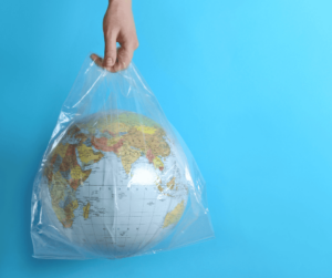 A hand holds a clear plastic bag with a globe inside in front of a solid blue background