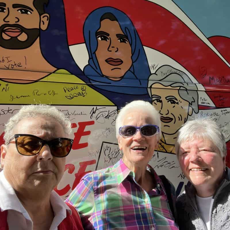 A selfie of three women with short, white hair standing in front of NETWORK's Nuns on the Bus tour bus