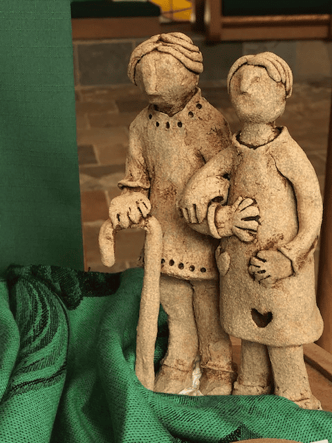 A tan sculpture of a man and a woman walking arm in arm sits on a green cloth