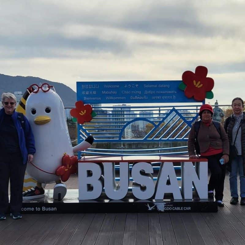 Sisters standing next to a sign for Busan, South Korea