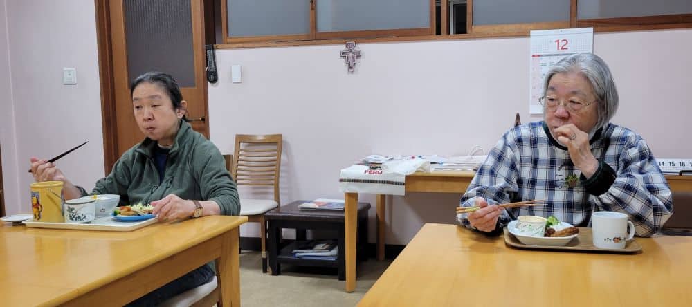 Two Japanese sisters eat a meal at separate tables side-by-side