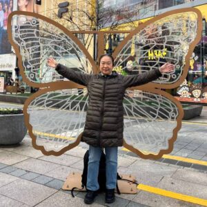 In a street in Busan, Sister Chizuru stands in front of a butterfly wing sculpture as is it is her own wings