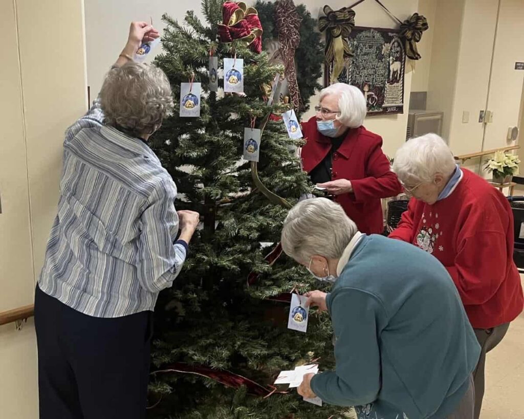 Four women hang Christmas ornaments on a tree