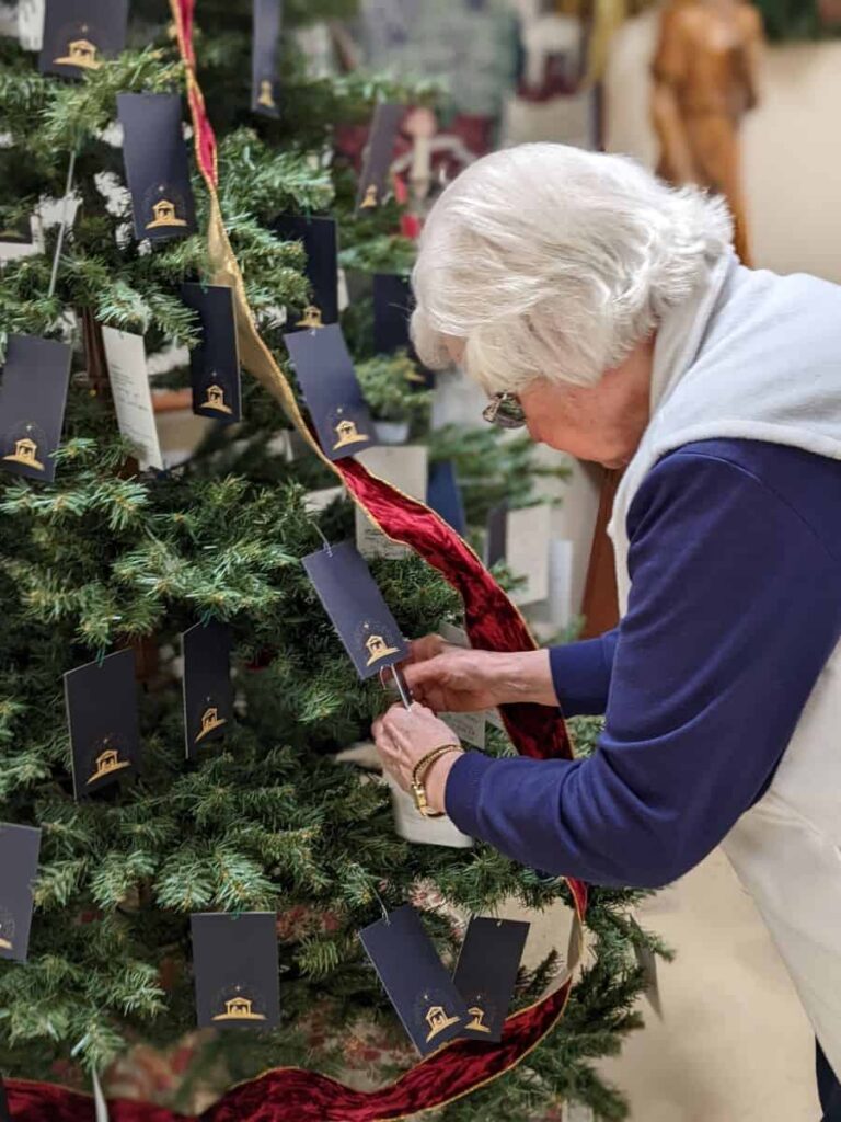 A woman with white hair places an ornament on a Christmas tree