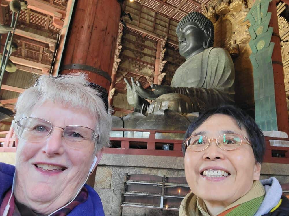 Two sisters take a selfie in front of a huge statue of Buddha