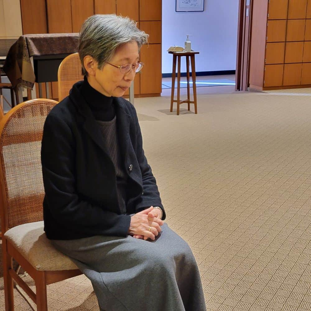 A Japanese sister sits quietly in a chair with her hands folded in her lap.