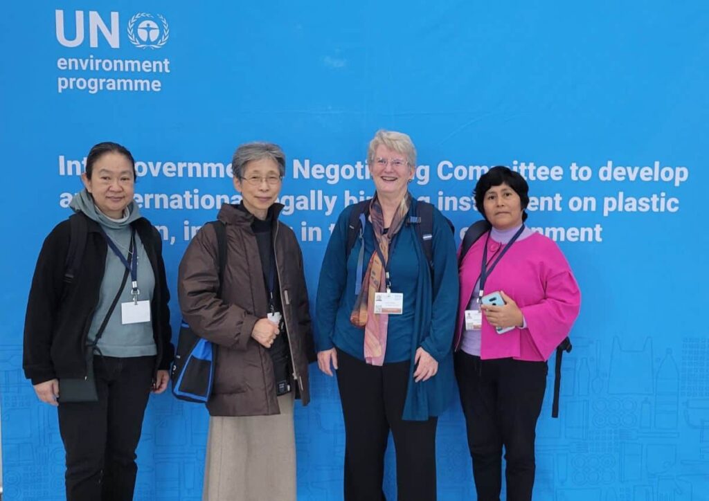 Four sisters stand together in front of a wall-to-wall sign for the UN negotiating session