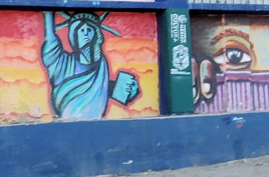 A brighly colored mural depicts the Statue of Liberty in front of a sunset on one half and eyes peering over a fence on the other half.