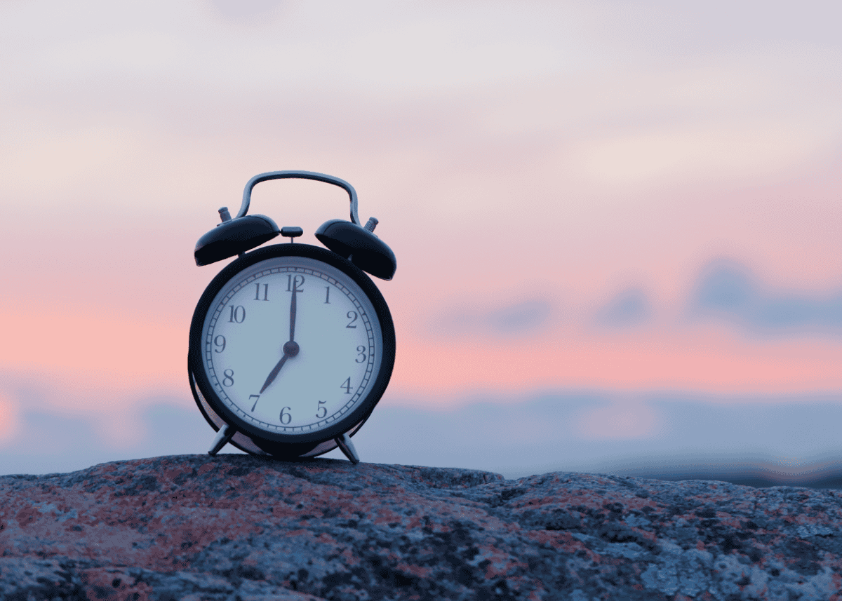 Photo of an alarm clock on a rock at sunrise