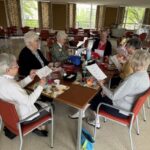 Seven women gathered around a table sharing a meal and preparing raffle tickets